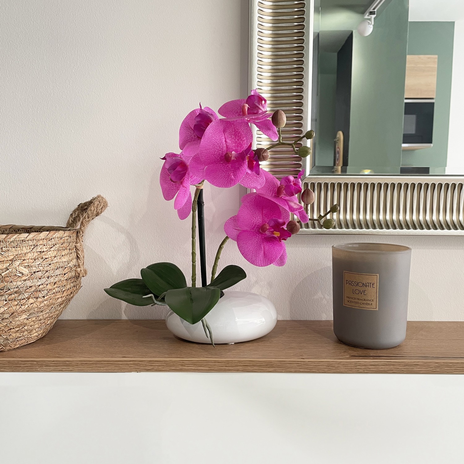 Orchidées artificielles fuchsia 35cm en ambiance sur une étagère entre une bougie et un cache-pot et à côté d'un miroir