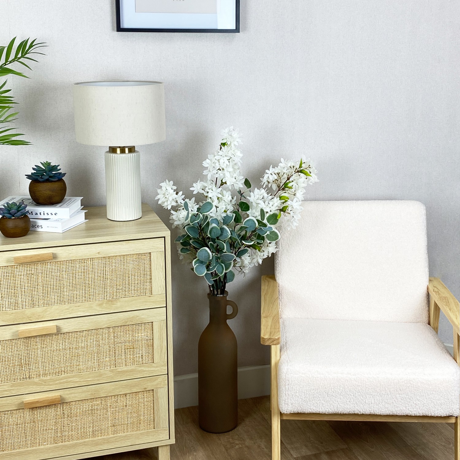 Jasmin artificiel en tige blanc 100cm lot de 2 dans un vase avec d'autres tiges à côté d'une commode et d'un fauteuil