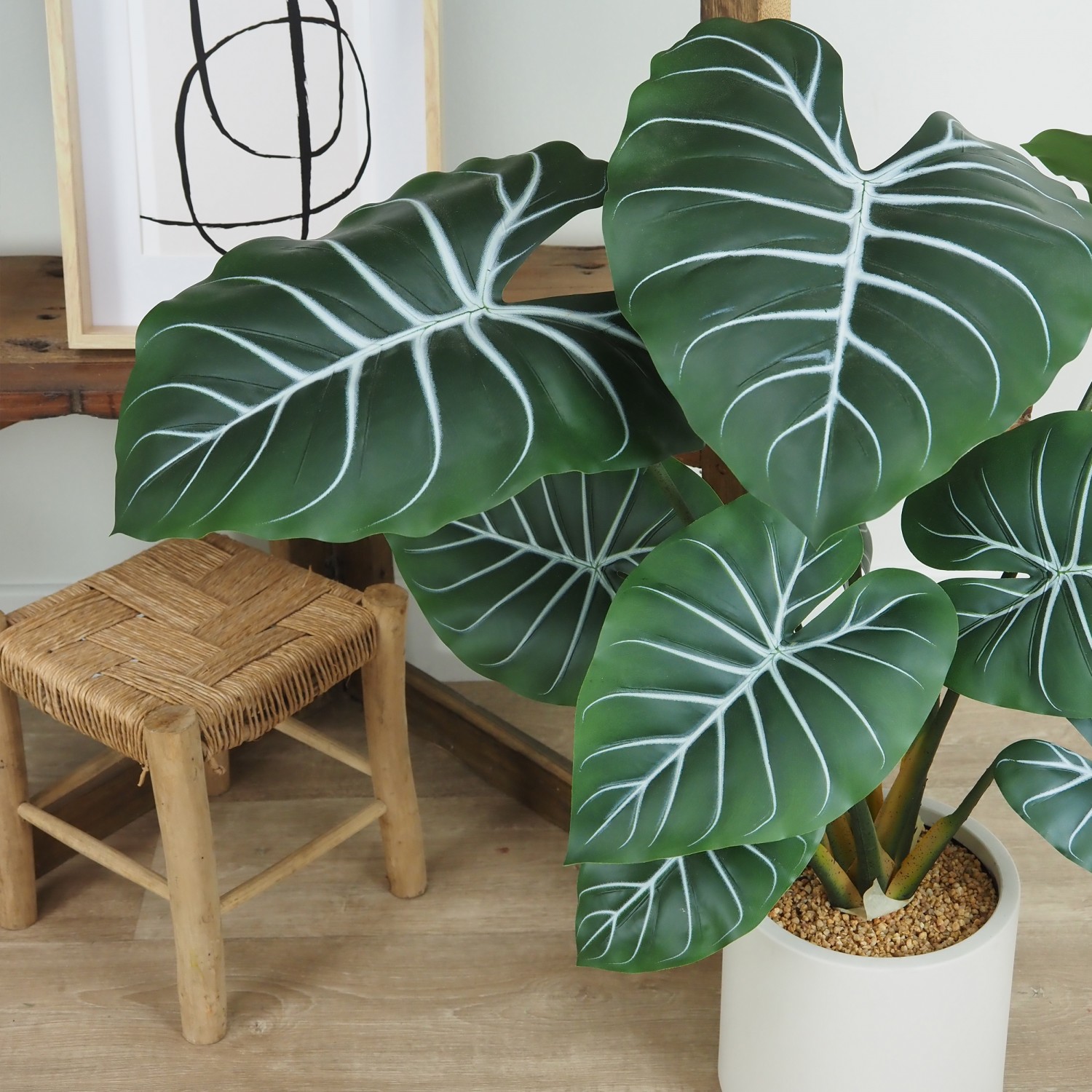 Plante taro artificiel 85cm posé au sol devant un meuble d'étagères avec de la déco focus zoom feuilles