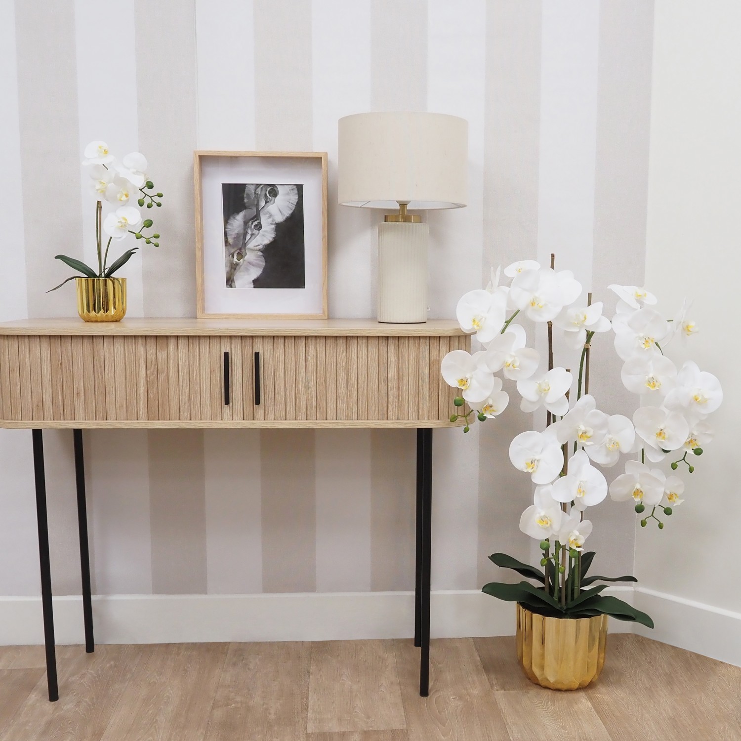 Orchidée artificielle toucher naturel pot or 40cm posée sur une console avec un cadre et une lampe
