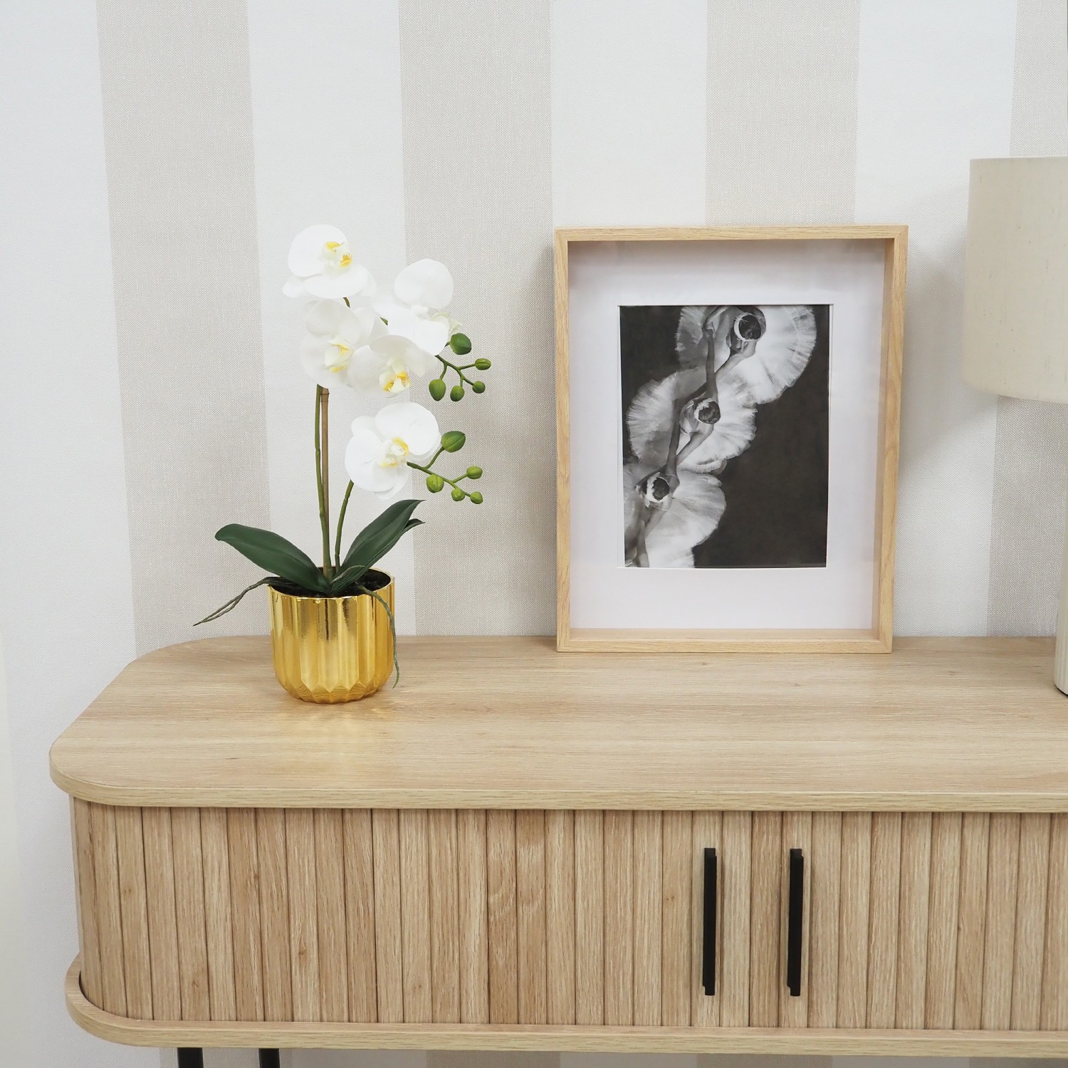 Orchidée artificielle toucher naturel pot or 40cm posée sur une console avec un cadre et une lampe focus zoom